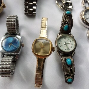 May include: A collection of five wristwatches with different styles and designs. The watches have silver, gold, and turquoise colored bands. One watch has a blue face with silver hands and numbers. Another watch has a white face with black hands and numbers. The third watch has a white face with black hands and Roman numerals. The fourth watch has a white face with black hands and numbers. The fifth watch has a white face with black hands and numbers.