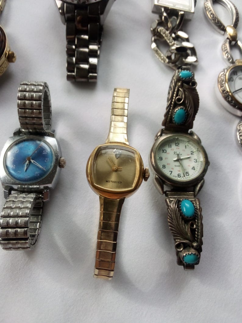 May include: A collection of five wristwatches with different styles and designs. The watches have silver, gold, and turquoise colored bands. One watch has a blue face with silver hands and numbers. Another watch has a white face with black hands and numbers. The third watch has a white face with black hands and Roman numerals. The fourth watch has a white face with black hands and numbers. The fifth watch has a white face with black hands and numbers.