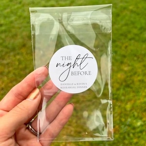 May include: A clear plastic bag with a white circle sticker that says "THE night BEFORE Danielle & Kevin's REHEARSAL DINNER" in black text.