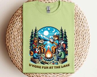 May include: A light green t-shirt with a cartoon illustration of animals gathered around a campfire. The animals are a bear, a raccoon, a fox, and a badger. The text "S'more Fun at the Lake" is printed on the bottom of the shirt.
