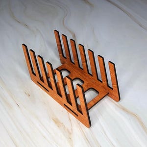 May include: A wooden plate rack with 10 slots for holding plates. The rack is made of natural wood with a reddish-brown stain.