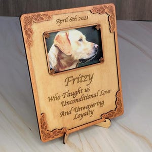 May include: A wooden photo frame with a picture of a dog and the text "April 6th 2021", " Fritzy", "Who Taught us Unconditional Love And Unwavering Loyalty".