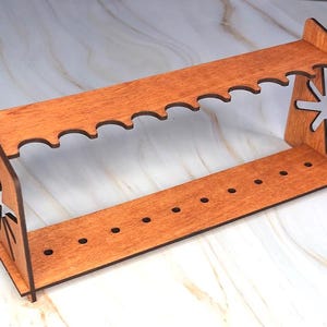 May include: A wooden stand with two tiers for holding pens or pencils. The stand has a decorative star-shaped cutout on the side and is made of light brown wood.