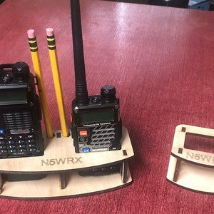 May include: Two black handheld radios with antennas, two yellow pencils, and a wooden stand with the text "N5WRX".