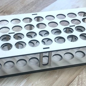 Op de afbeelding: Een houten reageerbuisrek met 48 gaten om reageerbuizen vast te houden. Het rek is gemaakt van lichtbruin hout en heeft een zwarte rand.