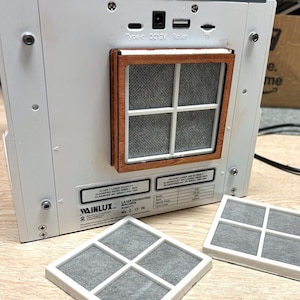 Könnte beinhalten: Eine weiße Lasergravurmaschine mit einem Holzrahmen um die Lüftung. Die Maschine hat ein Netzkabel und einen USB-Anschluss. Die Maschine ist mit "MAINLUX" und "LASER ENGRAVING MACHINE" beschriftet.