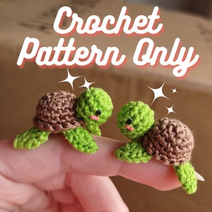 May include: Two small crocheted turtle amigurumi toys with brown shells and green bodies. The turtles have black eyes and pink mouths. The toys are sitting on a finger.