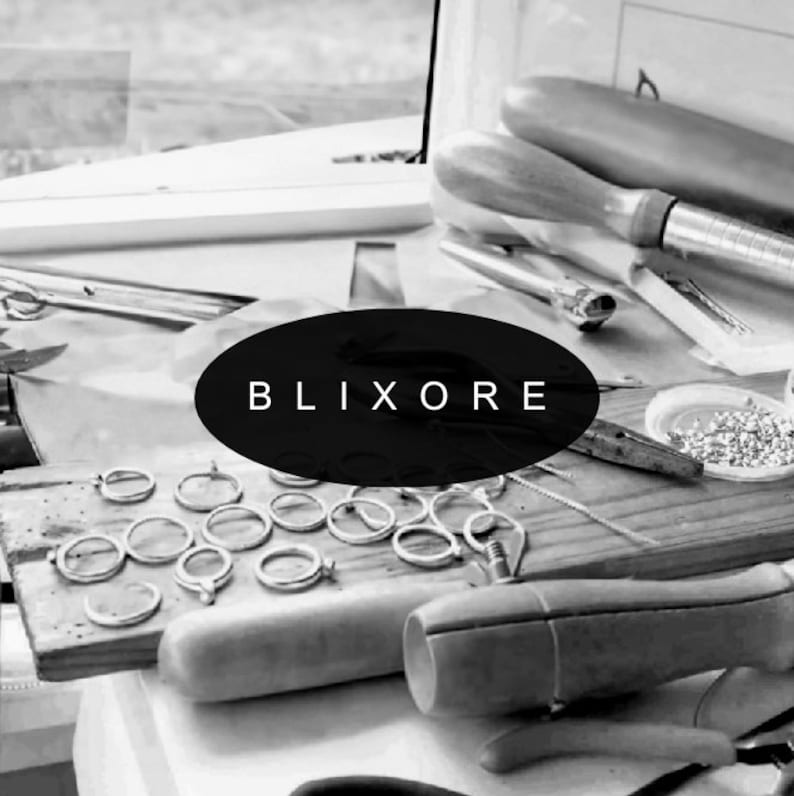 May include: A workbench with jewelry-making tools and materials. The word "BLIXORE" is displayed on a black oval. Silver rings are arranged on a wooden board, alongside pliers, a mandrel, and other tools.