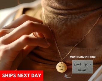 May include: Gold necklace with a round pendant that says "love you mom" in handwritten script. The pendant is shown next to a handwritten note that says "love you mom".