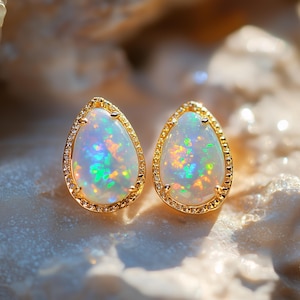 May include: A pair of opal earrings with a teardrop design. Each earring has a gold setting with small diamonds, surrounding an opal with iridescent colours. The opals show blue, green, and orange hues.