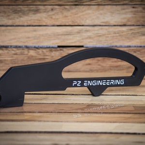 Könnte beinhalten: Schwarzes Metallwerkzeug mit einem gebogenen Griff und einer Aussparung. Das Werkzeug trägt den Schriftzug "PZ ENGINEERING".
