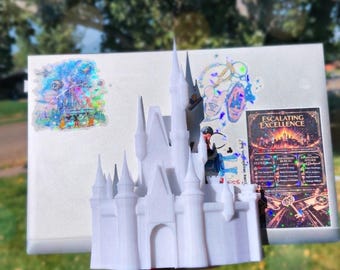 Peut inclure: Un modèle de château imprimé en 3D blanc placé devant un ordinateur portable argenté. Le couvercle de l'ordinateur présente un autocollant holographique de château, un petit autocollant circulaire et un rectangle avec le texte Escalating Excellence.
