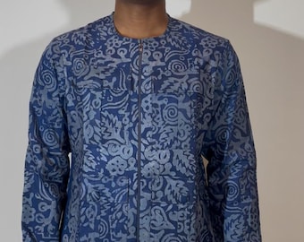 Op de afbeelding: Een jas met lange mouwen voorzien van een donkerblauw en lichtblauw patroon met herhalende motieven van krullen en bladeren. De jas heeft een ronde halslijn, een ritssluiting over de gehele voorzijde en twee rechthoekige borstzakken.