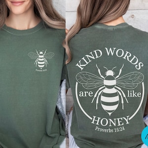 Może przedstawiać: Oliwkowo-zielona koszulka z białym wzorem pszczoły z przodu i z tyłu. Tył koszulki zawiera napis "KIND WORDS are like HONEY" z ilustracją pszczoły. Tekst "Przysłów 16:24" jest również dołączony.