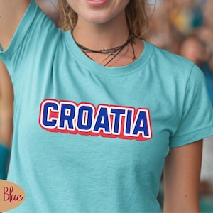 May include: Lagoon blue t-shirt with the word "CROATIA" in bold, white letters with a red outline and a blue shadow. The shirt is short-sleeved and appears to be made of a soft material.