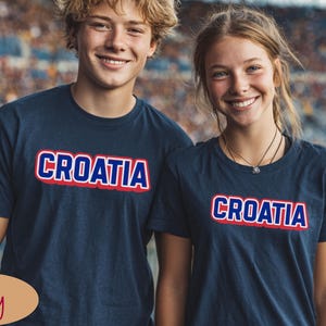 May include: Navy blue t-shirts with the word "CROATIA" in white letters with a red outline. The t-shirts are worn by two people, a young man and a young woman, who are smiling at the camera.