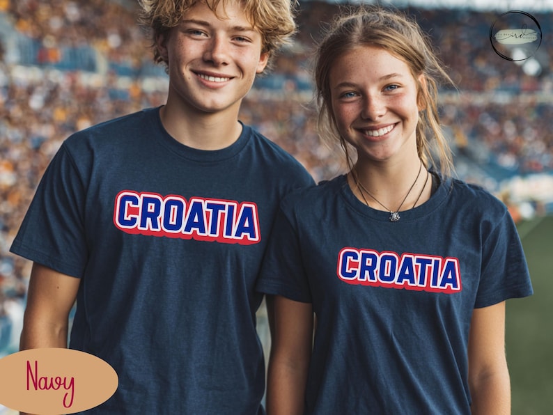 May include: Navy blue t-shirts with the word "CROATIA" in white letters with a red outline. The t-shirts are worn by two people, a young man and a young woman, who are smiling at the camera.