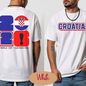May include: White t-shirt with the word "CROATIA" in red and blue lettering. The back of the shirt features the numbers "2026" in blue and red, with a Croatian flag graphic and the text "WORLD CUP CAN MEX USA".