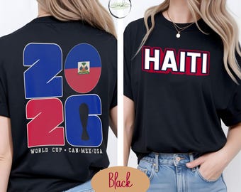 May include: Black t-shirt featuring the word "HAITI" in white letters with a red border. The shirt also displays "2026" in blue and red, with the Haitian flag incorporated. The text "WORLD CUP CAN MEX USA" is also visible.