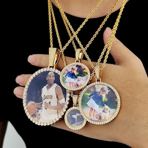 Puede incluir: Cuatro cadenas de oro con colgantes redondos para fotos. Los colgantes están incrustados con piedras de circonita cúbica transparentes. Las fotos en los colgantes incluyen un jugador de baloncesto, una niña pequeña con un perro y otras dos fotos.