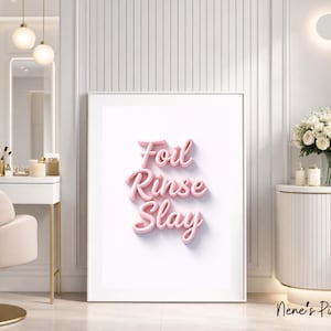 Op de afbeelding: Een ingelijste print met de roze tekst "Foil Rinse Slay" in 3D-letters. Het kunstwerk wordt gepresenteerd in een heldere, moderne salonsetting met een kaptafel, stoel en decoratieve accenten. De algehele esthetiek is strak en stijlvol.