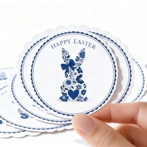 May include: White, scalloped-edge circular decorations with a blue floral bunny design and the words "HAPPY EASTER". The bunny is filled with blue flowers and a blue bow. Several decorations are visible.