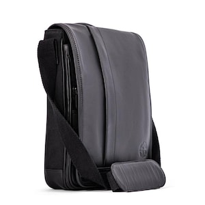 May include: A black leather messenger bag with a zipped pocket and an adjustable shoulder strap. The bag has a logo on the front.