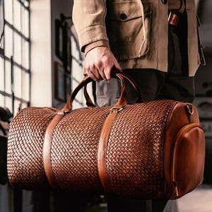 May include: A brown leather duffel bag with a woven pattern and a smaller zippered pocket on the side.