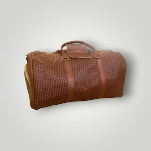 May include: A brown leather woven duffel bag with gold hardware and a zippered pocket on the side.