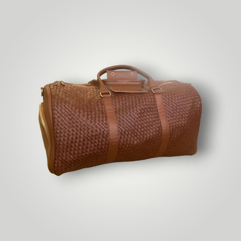 May include: A brown leather woven duffel bag with gold hardware and a zippered pocket on the side.