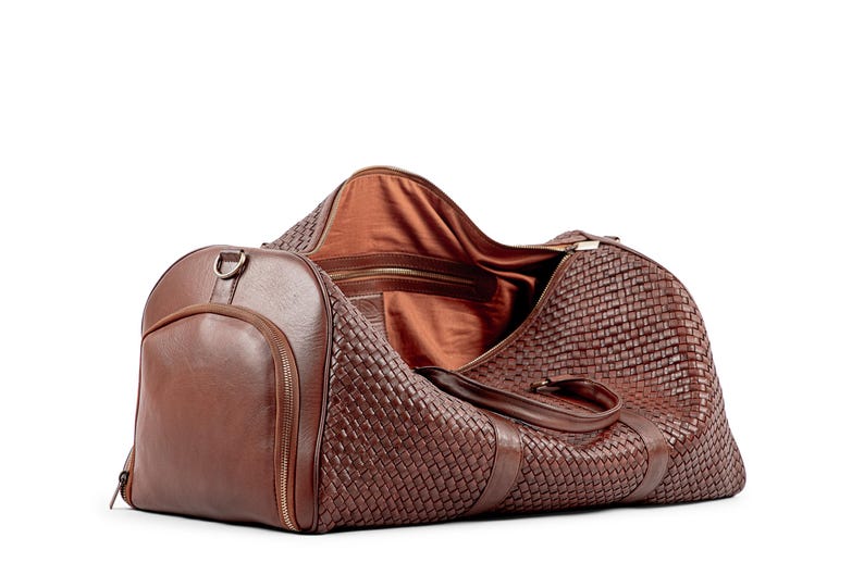 May include: A brown leather woven duffel bag with a zippered closure and a large pocket on the side.