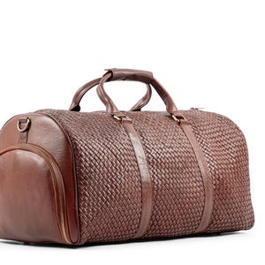 May include: A brown leather duffel bag with a woven pattern and a top handle. The bag has a zipper closure and a side pocket.
