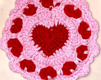 May include: A pink and red crocheted doily with a large heart in the center and smaller hearts around the edge.