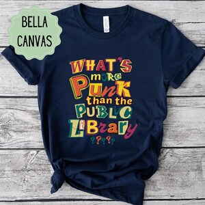 May include: A navy blue t-shirt with the text "What's more punk than the public library????" in colourful, stylised letters.