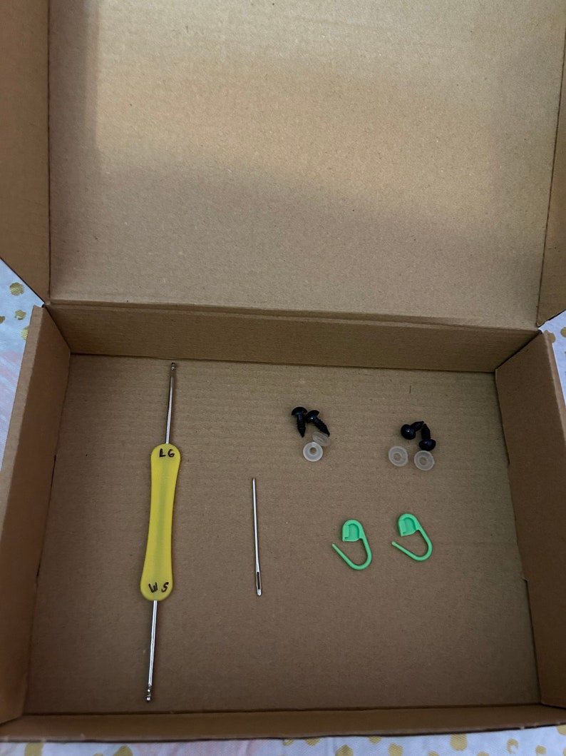 K&ouml;nnte beinhalten: Ein Karton mit einer gelben Stricknadel, einer silbernen Nadel, zwei gr&uuml;nen Sicherheitsnadeln und zwei Paaren schwarzer Kunststoff-Sicherheitsaugen mit wei&szlig;en Unterlegscheiben.