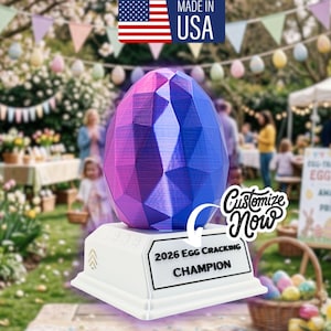 May include: A geometric, multi-colored egg-shaped trophy with a white base. The trophy reads "2026 Egg Cracking Champion." The image includes the text "Made in USA" and "Customize Now." The background shows an outdoor Easter event.