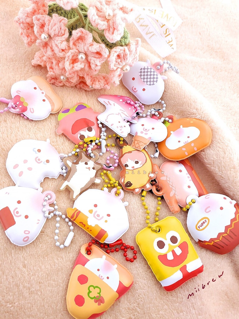 May include: A collection of colorful, cartoon-themed keychains featuring various characters and designs. The keychains are made of soft, squishy material and have a variety of shapes, including a mushroom, a banana, a cupcake, and a pizza slice. The keychains are attached to silver chains.
