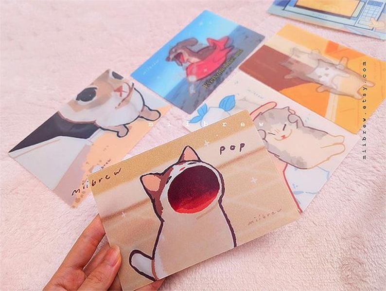 May include: Set of five illustrated greeting cards featuring cute cartoon cats with different expressions. The cards are printed on white cardstock with a light brown background and have a matte finish. The text on the cards reads "Pop" and "Milbrew".