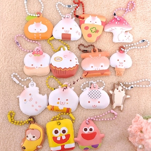 May include: A collection of 14 colorful keychains featuring various cartoon characters and food designs. The keychains are made of soft, plush material and have a variety of colors, including pink, yellow, blue, green, and brown. The keychains are attached to silver chains.