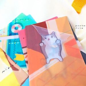 May include: A stack of colorful patterned plastic folders with a clear protective film on top. The top folder features a cartoon cat illustration.
