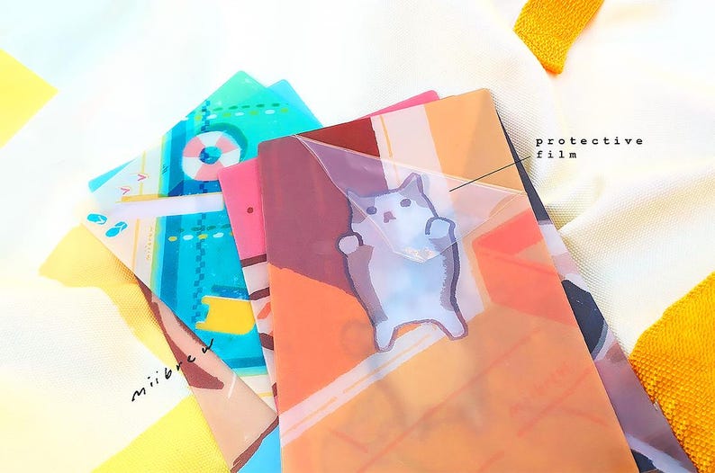 May include: A stack of colorful patterned plastic folders with a clear protective film on top. The top folder features a cartoon cat illustration.