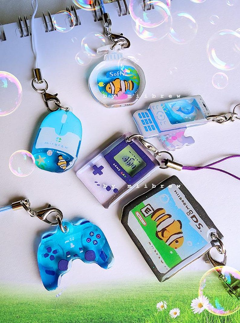 May include: A collection of clear acrylic charms with various designs, including a mouse, a controller, a game console, and a fish in a bubble. Each charm has a silver clasp and a lanyard for attachment.