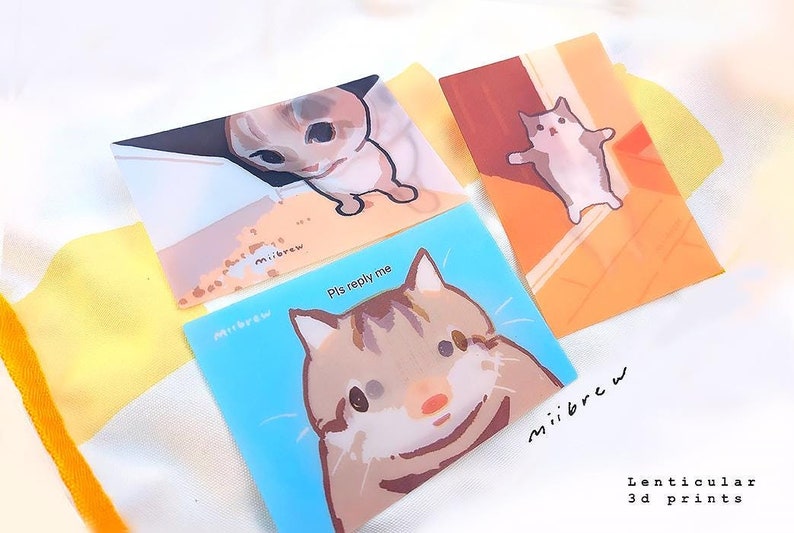 May include: Three lenticular 3D prints featuring cats. The first print shows a cat looking down from a ledge. The second print shows a cat looking up with the text "Pls reply me". The third print shows a cat looking to the side. All prints have the text "miiibrew" on them.