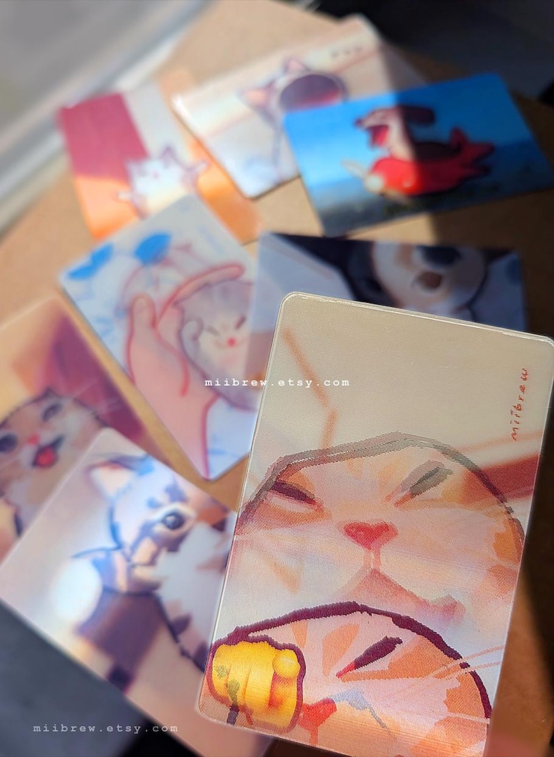 May include: A collection of rectangular cards featuring colorful illustrations of cats in various poses and settings. Each card displays a unique artistic depiction of a feline, with the text miibrew.etsy.com printed on the surfaces.