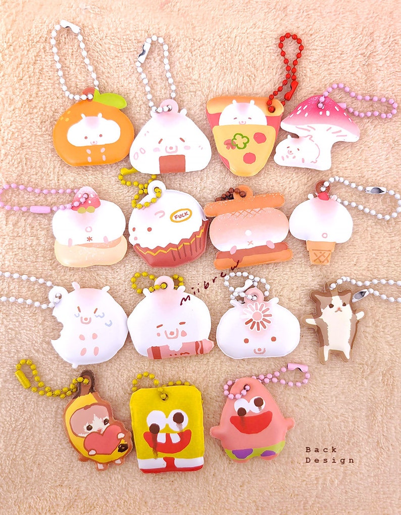 May include: A collection of 14 colorful keychains featuring various cartoon characters and designs. The keychains are made of soft, squishy material and have a variety of shapes, including a mushroom, a pizza slice, a cupcake, a hamburger, and a cat. The keychains are all attached to silver chains.
