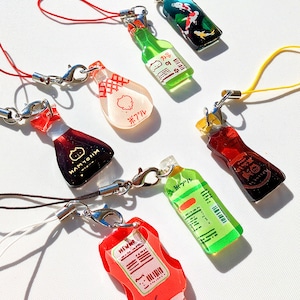 May include: A collection of colorful, miniature bottle charms with lobster clasp attachments. The charms feature various designs, including a koi pond, soy sauce, and ketchup. Each charm has a different colored cord.