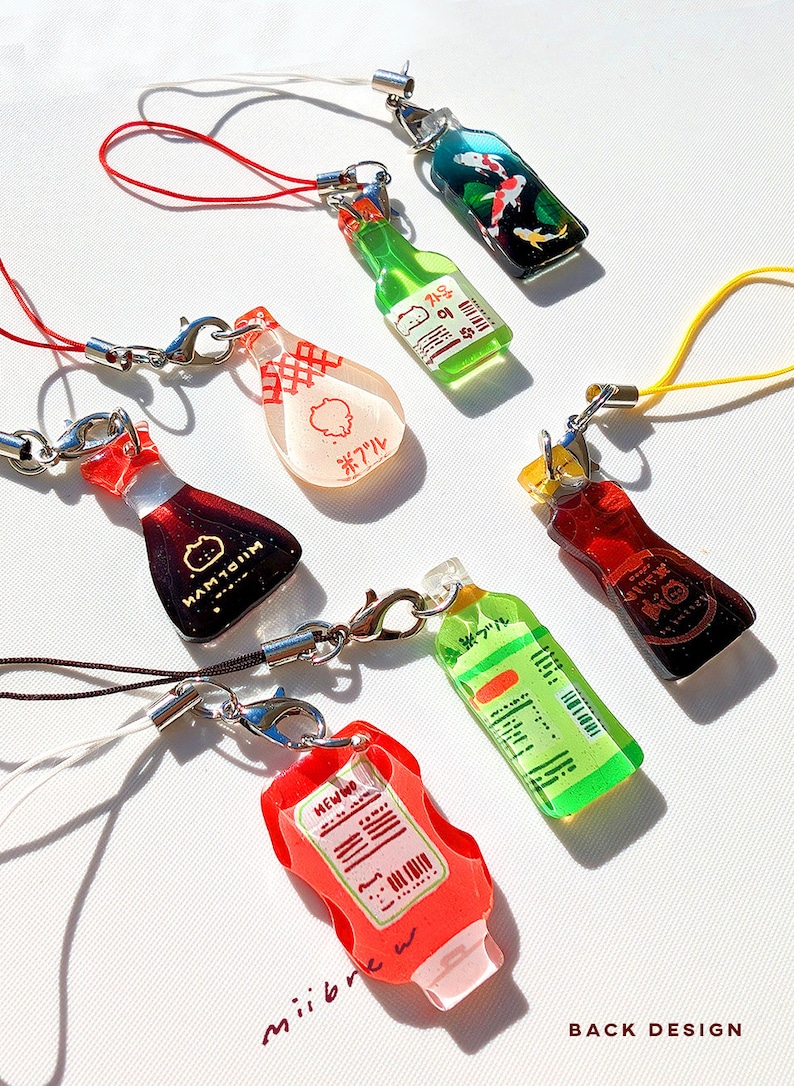 May include: A collection of colorful, miniature bottle charms with lobster clasp attachments. The charms feature various designs, including a koi pond, soy sauce, and ketchup. Each charm has a different colored cord.
