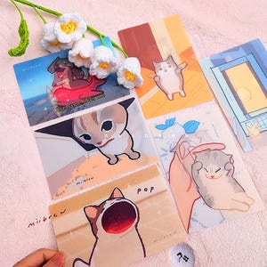 May include: A set of six colorful illustrated cards featuring cats with different expressions. The cards have a light background and are decorated with a variety of colors and patterns. The cards are perfect for adding a touch of whimsy to any space.