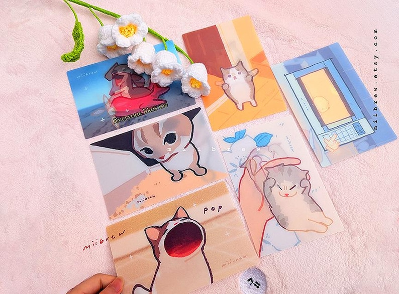 May include: A set of six colorful illustrated cards featuring cats with different expressions. The cards have a light background and are decorated with a variety of colors and patterns. The cards are perfect for adding a touch of whimsy to any space.