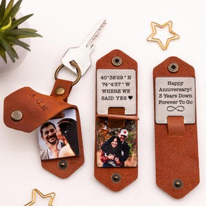 Pode incluir: Um chaveiro de couro marrom com um inserto para fotos e uma etiqueta de metal gravada com coordenadas e as palavras "Where We Said Yes". A etiqueta de metal do lado direito est&aacute; gravada com "Happy Anniversary! 3 Years Down Forever To Go".